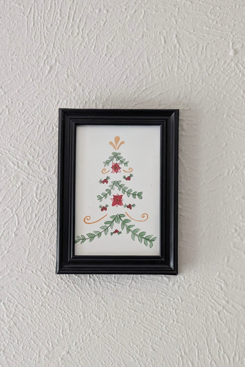 a framed print of a watercolor and pen painting of a folk art inspired christmas tree hangs on a wall
