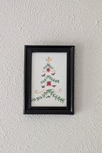 a framed print of a watercolor and pen painting of a folk art inspired christmas tree hangs on a wall