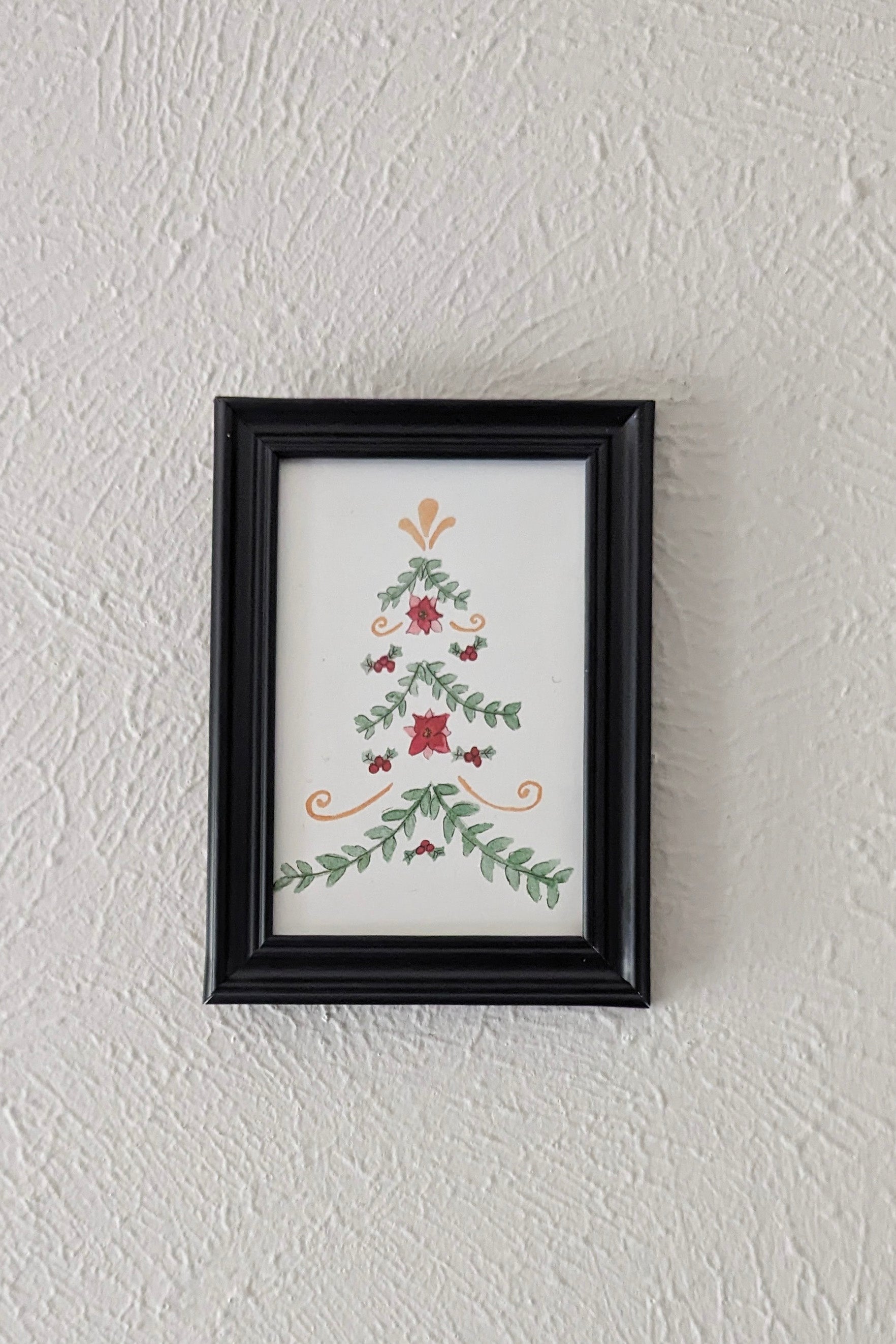 a framed print of a watercolor and pen painting of a folk art inspired christmas tree hangs on a wall